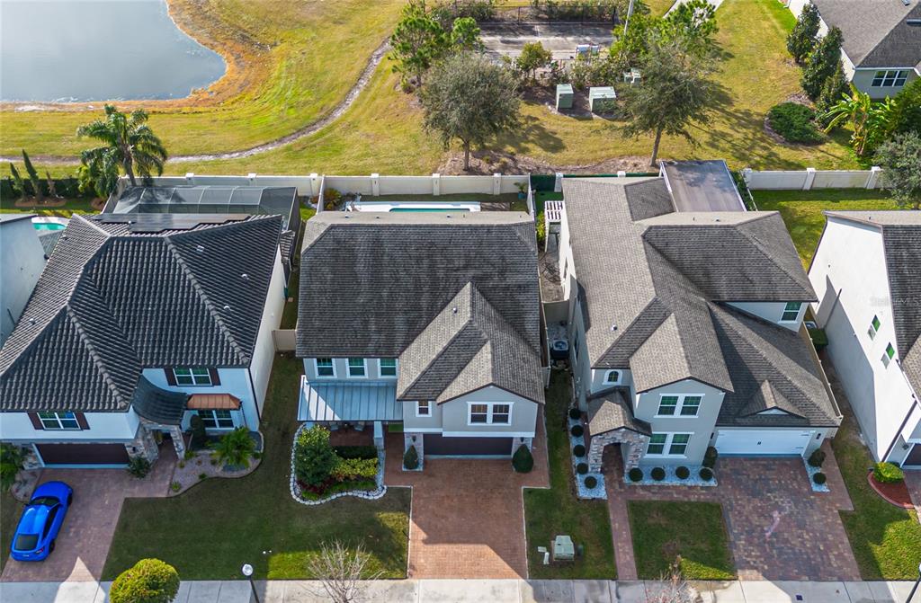An aerial view shows three suburban houses with tiled roofs and paved driveways near a pond — 3310 STONEWYCK STREET, ORLANDO, FL