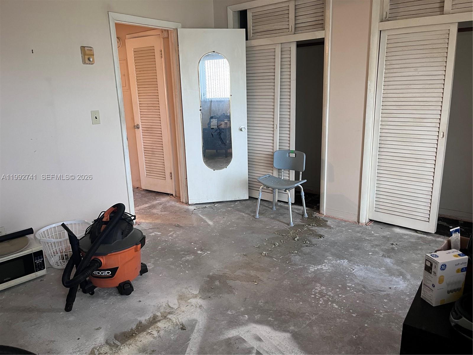 An unfinished room features a concrete floor, a shop vacuum, and several louvered doors — 1012 SW 11th St # 9N, Hallandale Beach FL 33009, HALLANDALE BEACH, FL