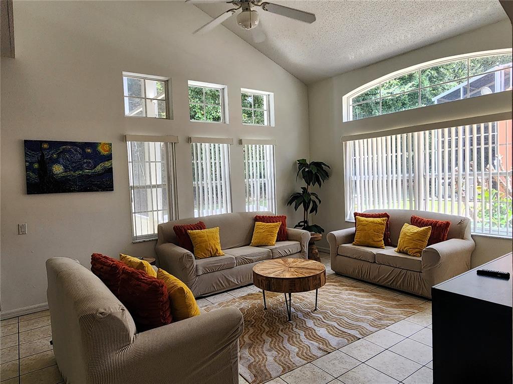 A living room features beige sofas, a wooden coffee table, tile floors, and large windows — 1013 PARK RIDGE CIRCLE, KISSIMMEE, FL