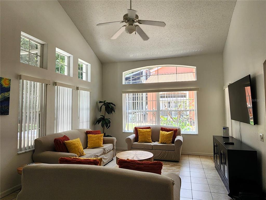 A living room features vaulted ceilings, tile floors, a ceiling fan, and multiple windows — 1013 PARK RIDGE CIRCLE, KISSIMMEE, FL