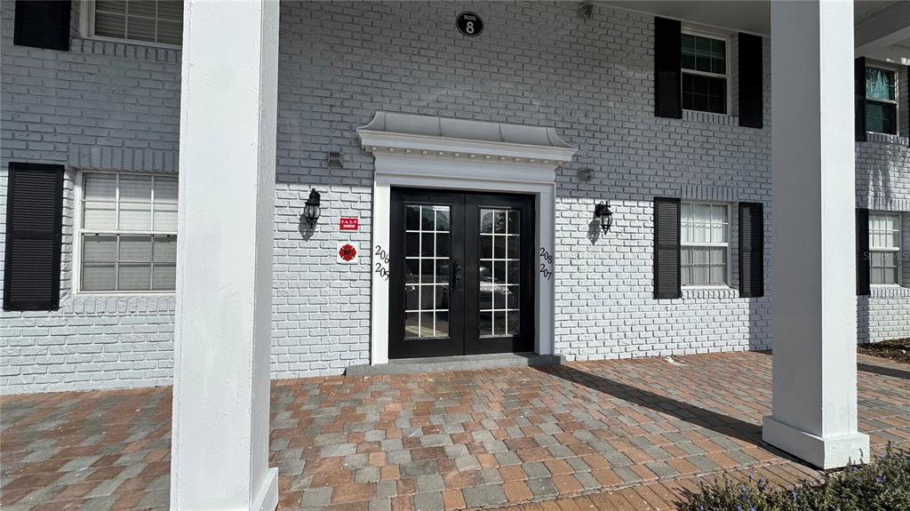 The exterior of a white brick building features a double-door entrance and a paved patio — 205 LEWFIELD CIRCLE UNIT 205, WINTER PARK, FL