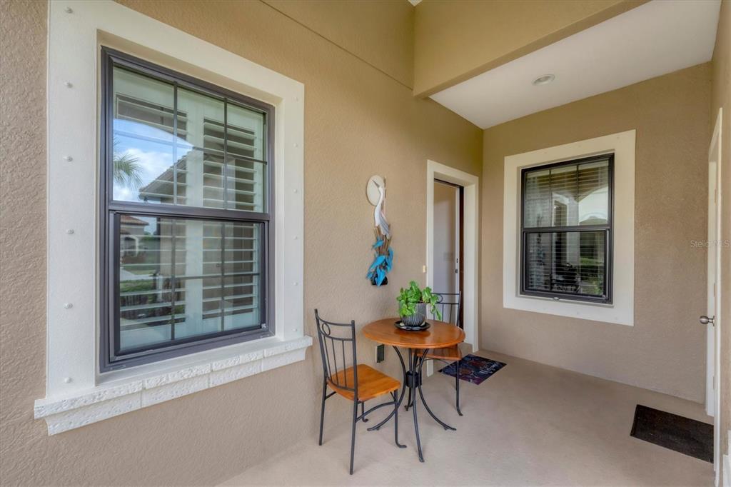 A covered patio features a small bistro table with two chairs and two windows — 317 ACERNO DRIVE, NOKOMIS, FL