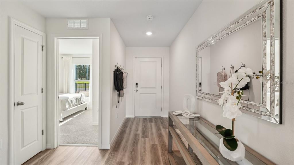 A hallway features wood-look flooring, a console table with a mirror, and a bedroom doorway — 8753 TRIUMPH CIRCLE, WILDWOOD, FL