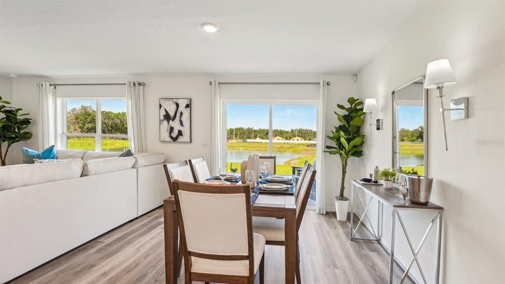A dining area with a wooden table and chairs overlooks a lake through sliding doors — 8753 TRIUMPH CIRCLE, WILDWOOD, FL