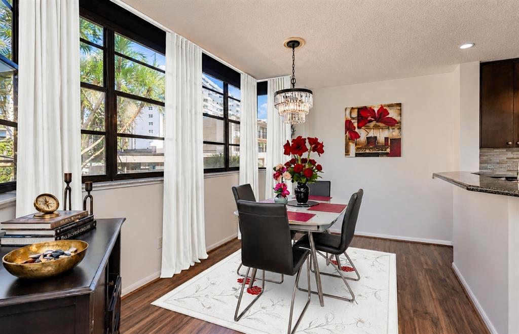 A dining area features a glass table, four black chairs, a chandelier, and large windows — 602 LIME AVENUE UNIT 203, CLEARWATER, FL
