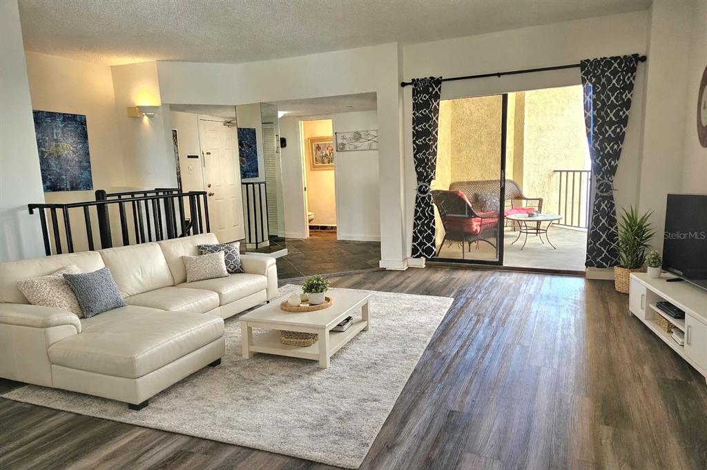 A living room with a white sectional sofa, wood-look flooring, and a sliding glass door — 602 LIME AVENUE UNIT 203, CLEARWATER, FL