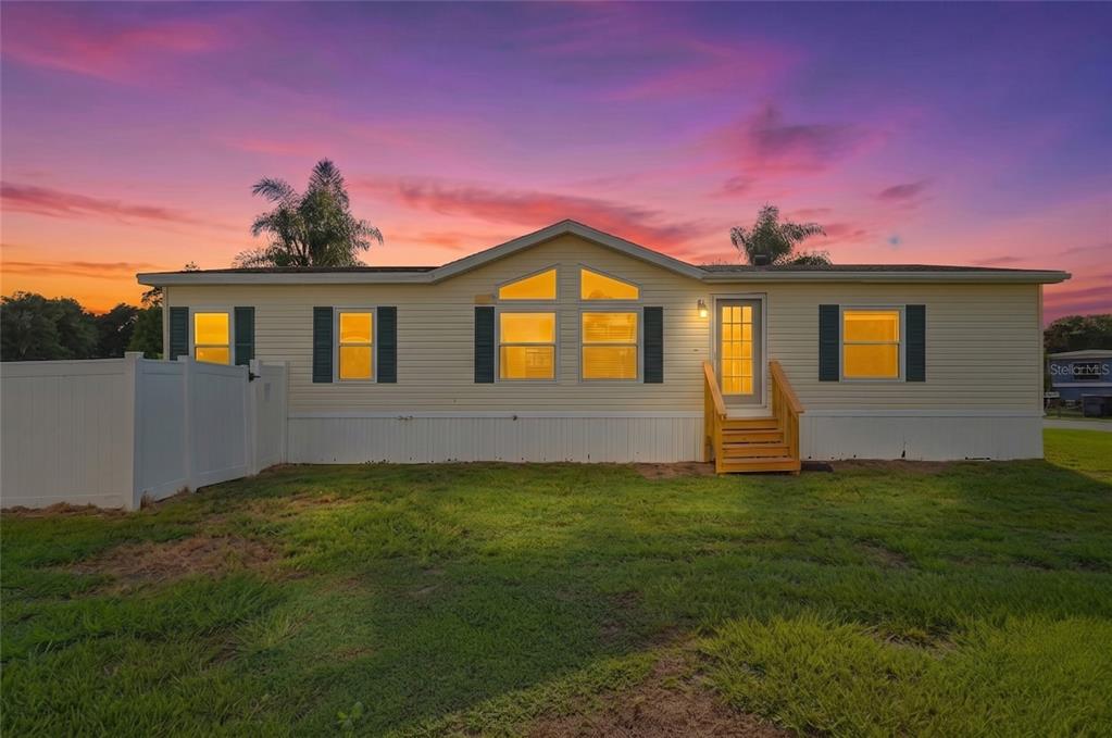 A yellow manufactured home with a gabled roof stands against a vibrant sunset sky — 338 1ST AVENUE N, LAKE WALES, FL