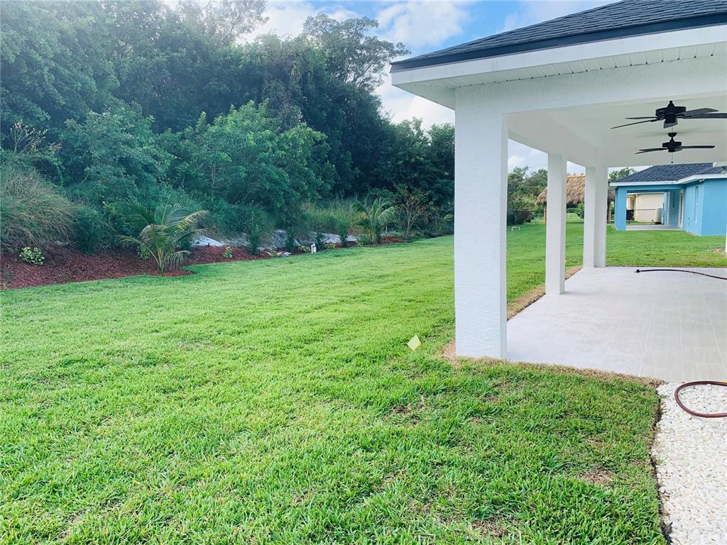 A covered patio overlooks a grassy backyard with a landscaped slope and dense trees — 120 CLINTON AVENUE, LAKE PLACID, FL