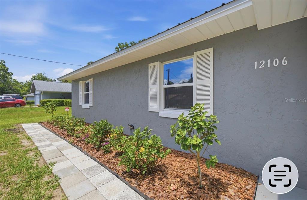 A gray house exterior features a stone walkway, landscaped garden beds, and white window shutters — 12106 SE 74TH TERRACE, BELLEVIEW, FL