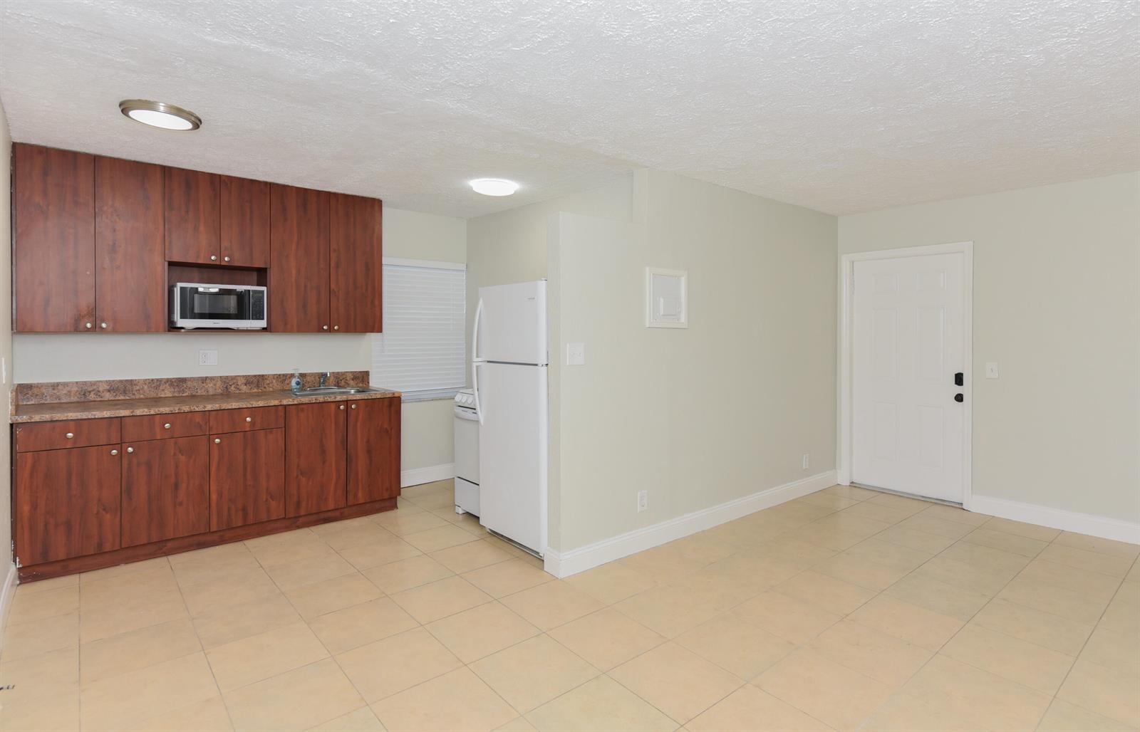 A kitchen features wood cabinets, a microwave, a sink, and a white refrigerator on tile flooring — 605 N Federal Highway # 8, FL 33460, FL
