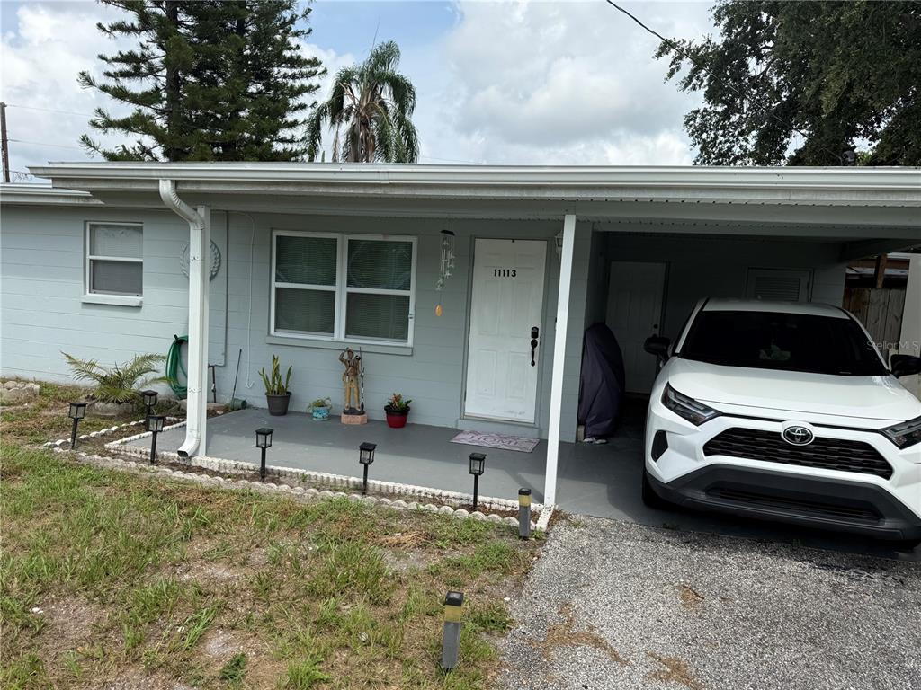 A light blue house exterior features a front porch, a carport, and a white car — 11113 102ND LANE, LARGO, FL