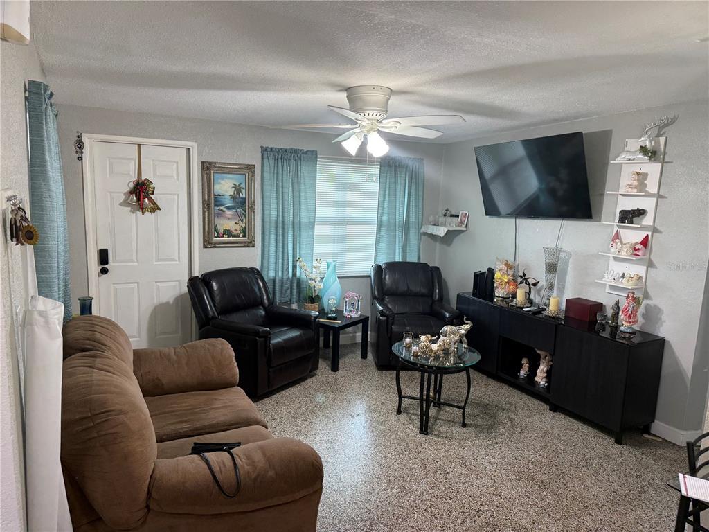 A living room features a brown sofa, two black recliners, a television, and terrazzo flooring — 11113 102ND LANE, LARGO, FL