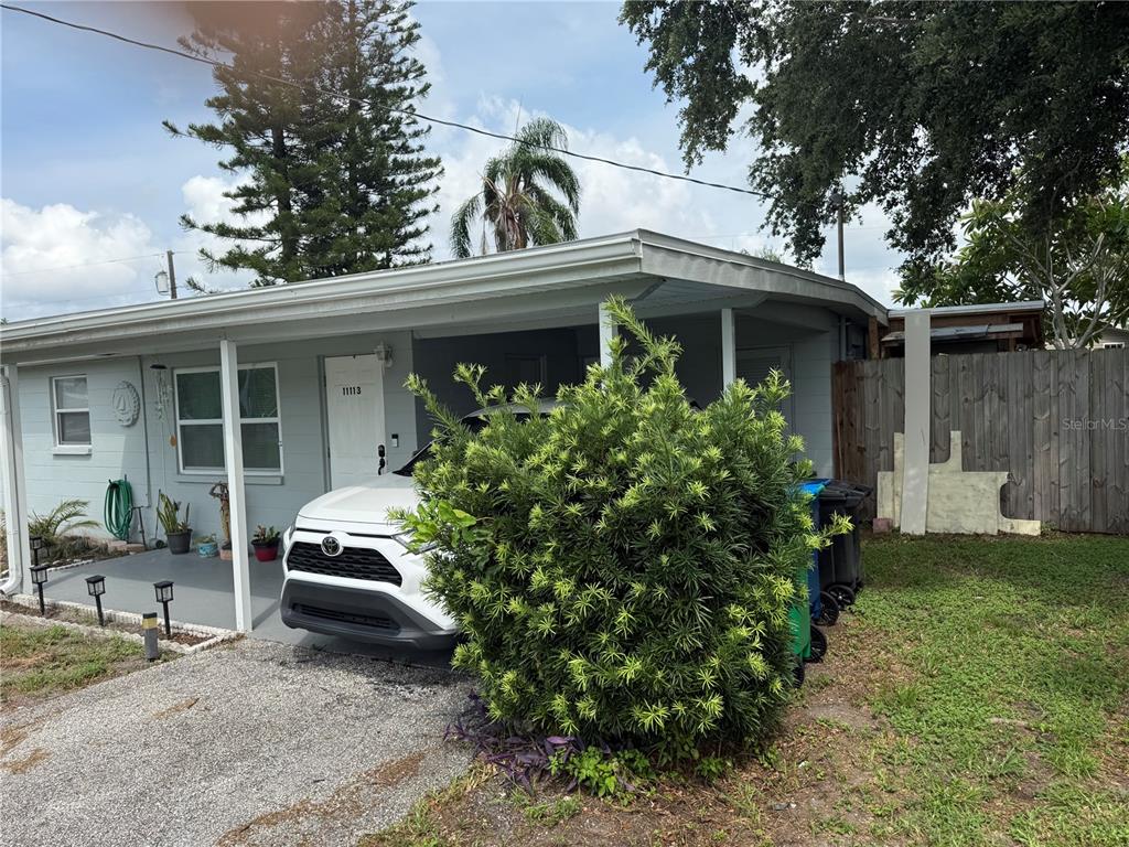 A white car is parked under a carport next to a house with a bush — 11113 102ND LANE, LARGO, FL