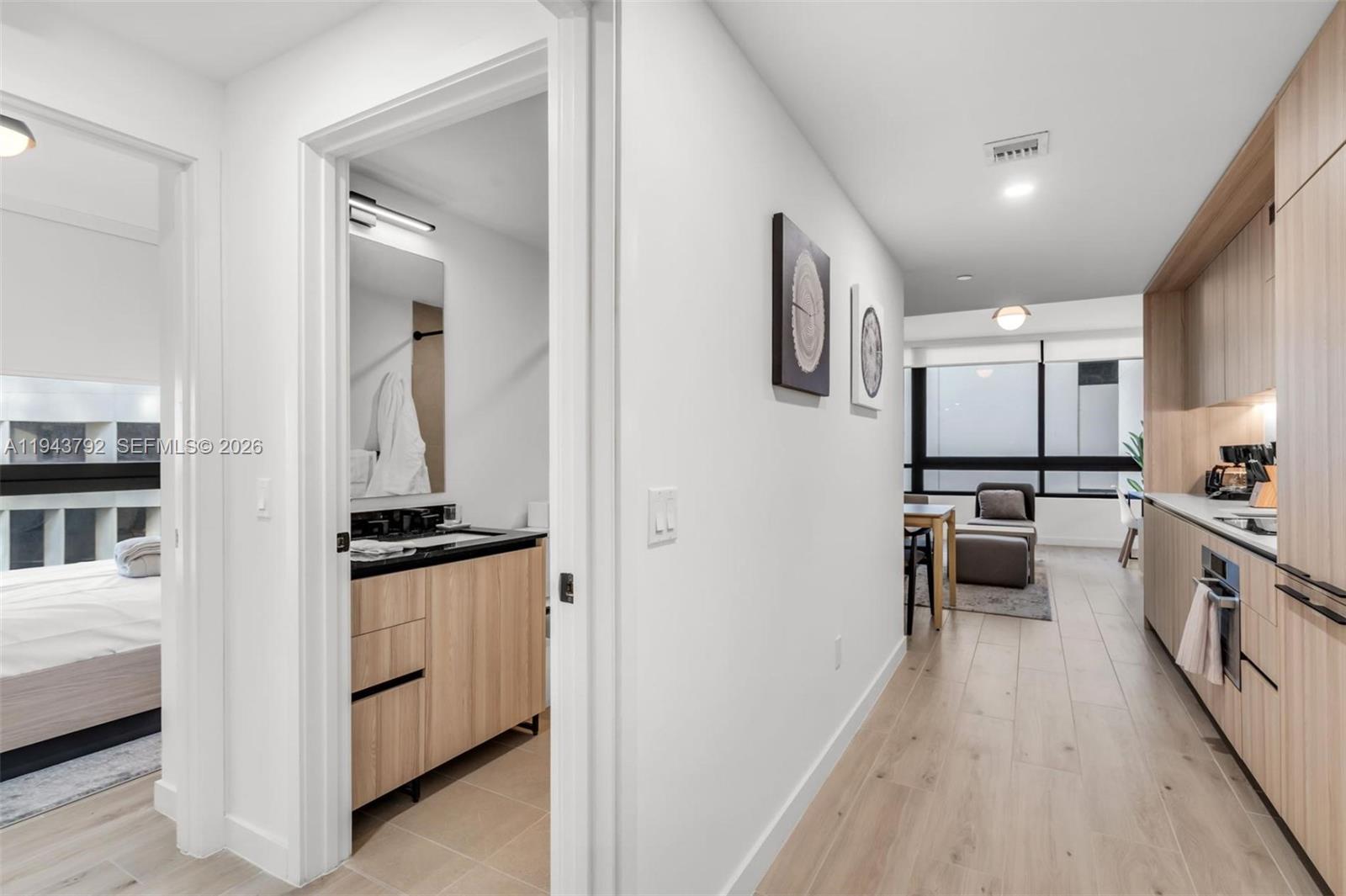 A hallway connects a bathroom with wood cabinetry to a kitchen and living area — 225 N Miami Ave # 301, Miami FL 33128, MIAMI, FL