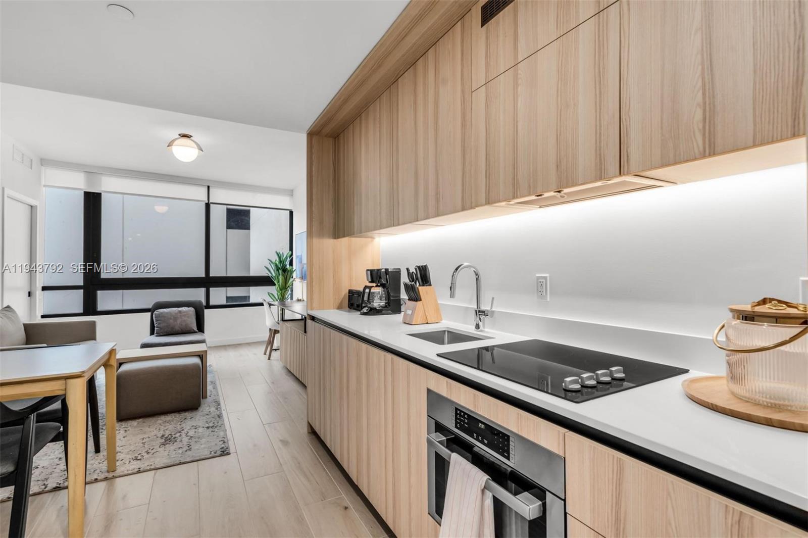 A modern kitchen with light wood cabinetry and white countertops opens into a living area — 225 N Miami Ave # 301, Miami FL 33128, MIAMI, FL