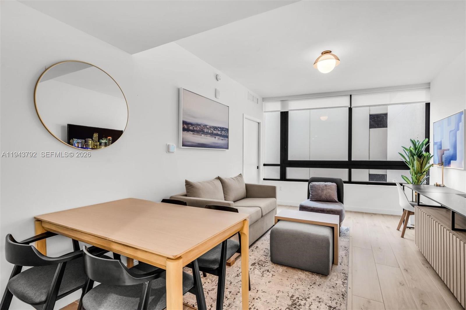 A living and dining area features a sofa, dining table, chairs, and large windows — 225 N Miami Ave # 301, Miami FL 33128, MIAMI, FL