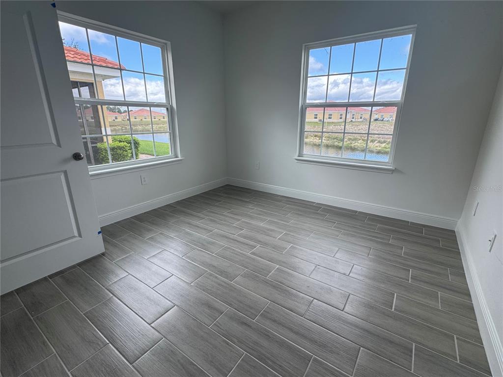 An empty room features gray wood-look tile flooring, white walls, and two windows overlooking water — 1602 CUMIN DRIVE UNIT 1602, POINCIANA, FL