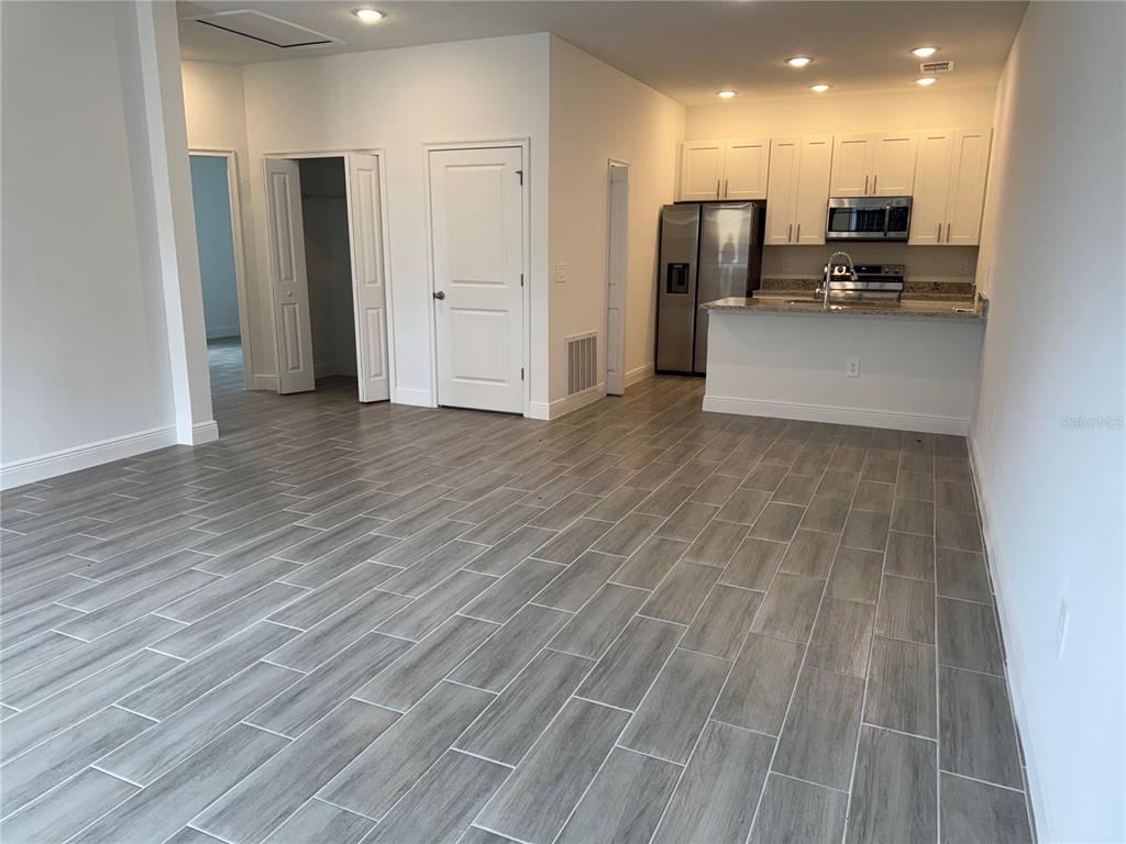 An open-concept kitchen and living area features gray wood-look tile flooring and white cabinetry — 1602 CUMIN DRIVE UNIT 1602, POINCIANA, FL