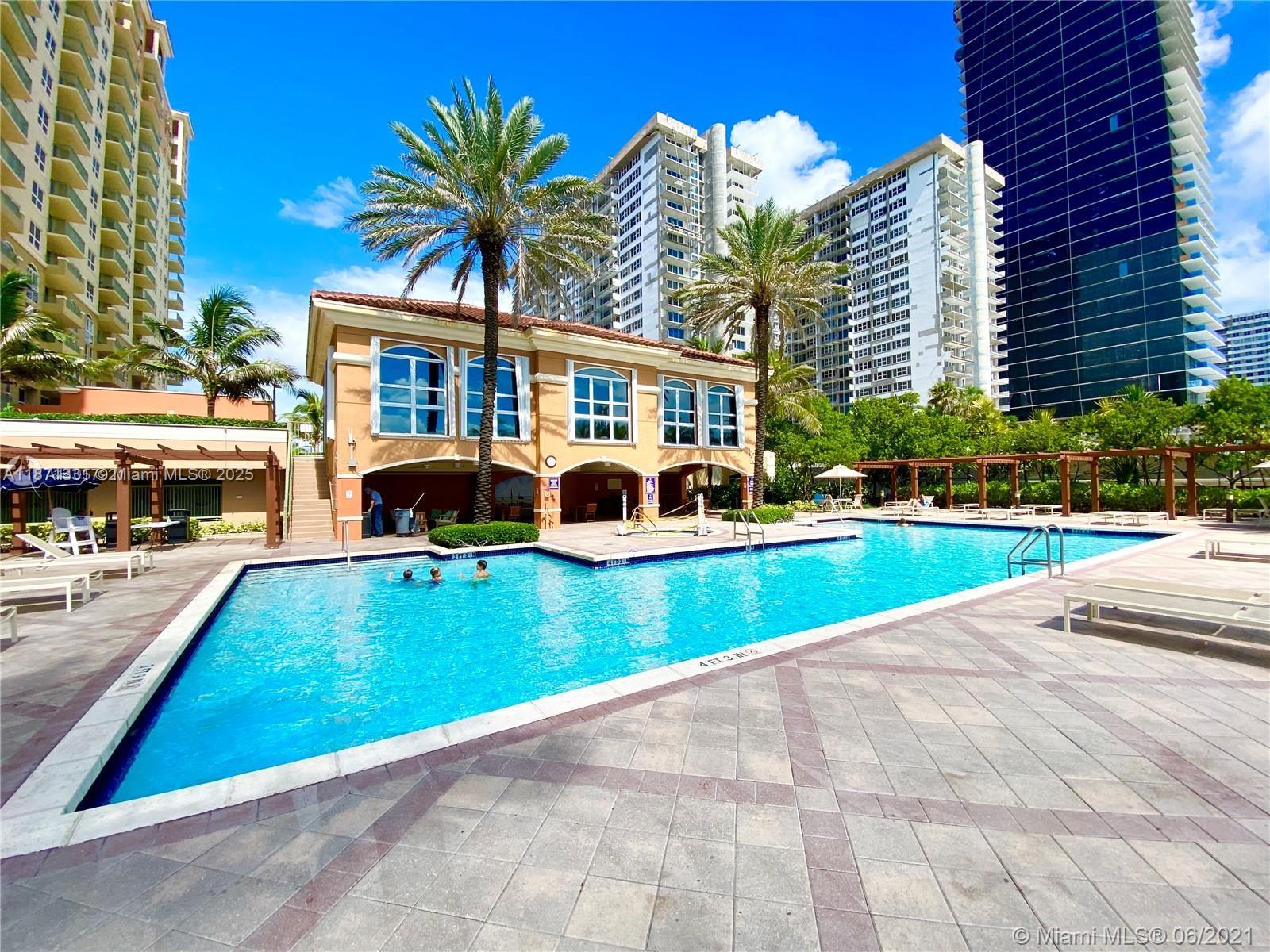 A swimming pool sits in front of a tan clubhouse building surrounded by tall towers — 2080 S Ocean Dr # 604, Hallandale Beach FL 33009, HALLANDALE BEACH, FL