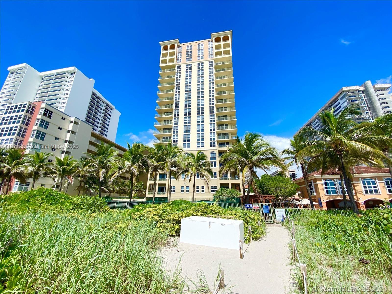 A tall residential building stands behind a sandy path surrounded by beach grass and palms — 2080 S Ocean Dr # 604, Hallandale Beach FL 33009, HALLANDALE BEACH, FL