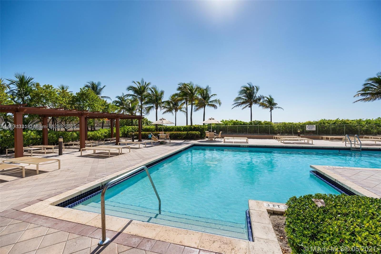 An outdoor swimming pool with a patio, lounge chairs, and palm trees under a clear sky — 2080 S Ocean Dr # 604, Hallandale Beach FL 33009, HALLANDALE BEACH, FL
