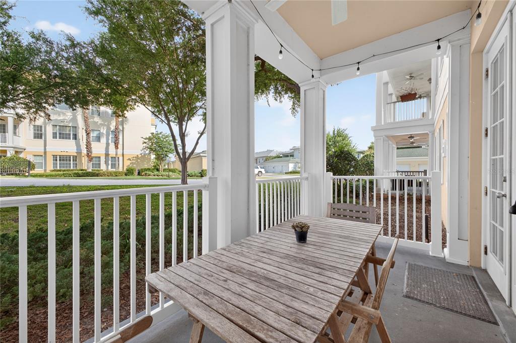 A covered outdoor patio features a wooden table, chairs, and white railings overlooking a lawn — 7521 MOURNING DOVE CIRCLE UNIT 103, REUNION, FL
