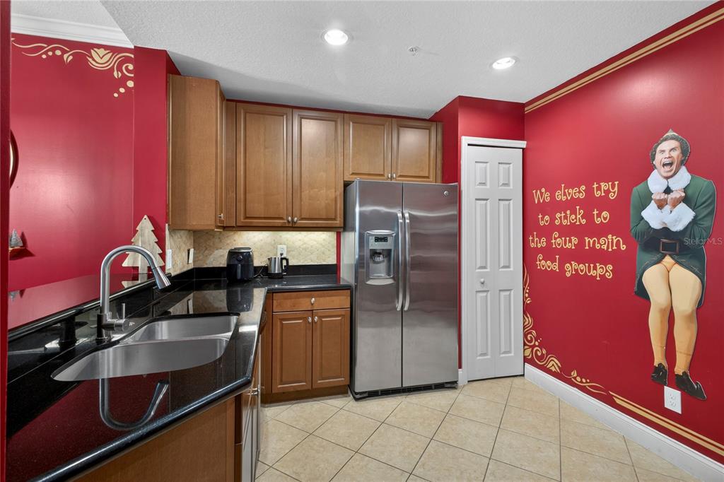 A kitchen features red walls, wood cabinets, black countertops, and a large Buddy the Elf decal — 7521 MOURNING DOVE CIRCLE UNIT 103, REUNION, FL