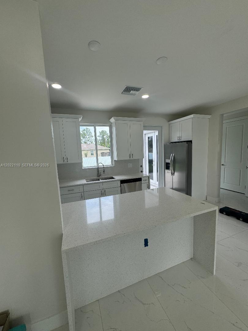 A modern kitchen features white cabinetry, a quartz island, and stainless steel appliances — 55 S Colin ave, Lehigh Acres FL 33976, LEHIGH ACRES, FL