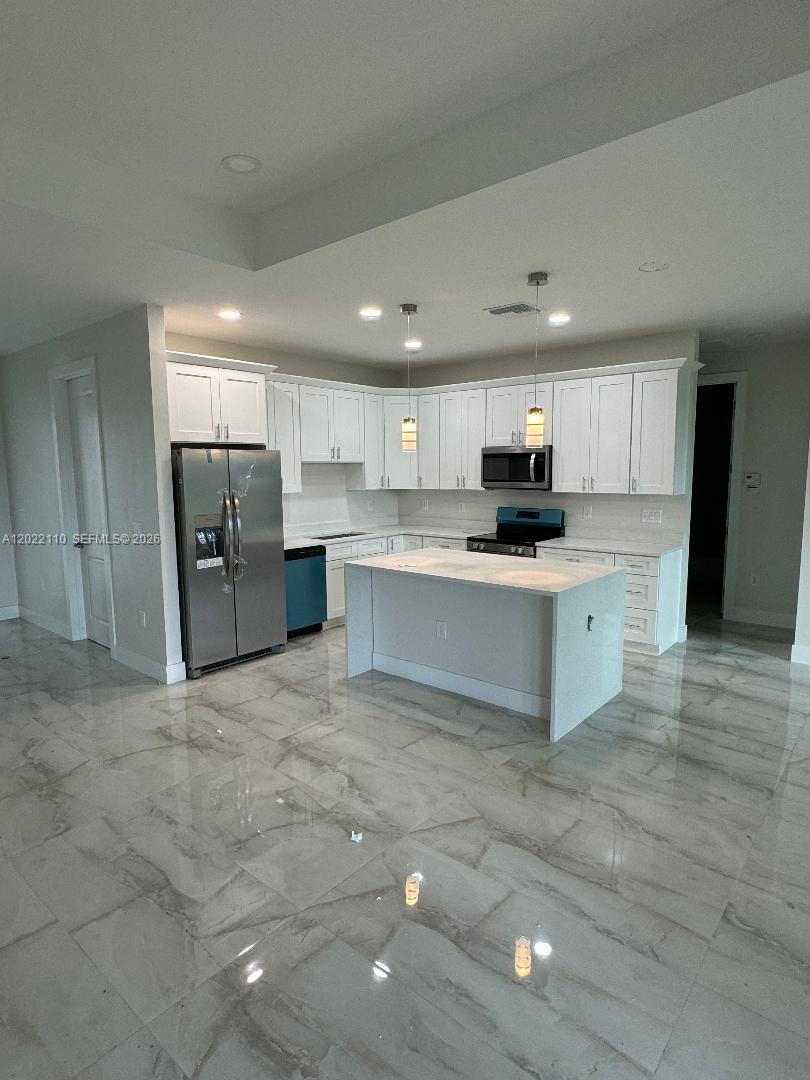A modern kitchen features white cabinetry, stainless steel appliances, a central island, and marble-look flooring — 55 S Colin ave, Lehigh Acres FL 33976, LEHIGH ACRES, FL