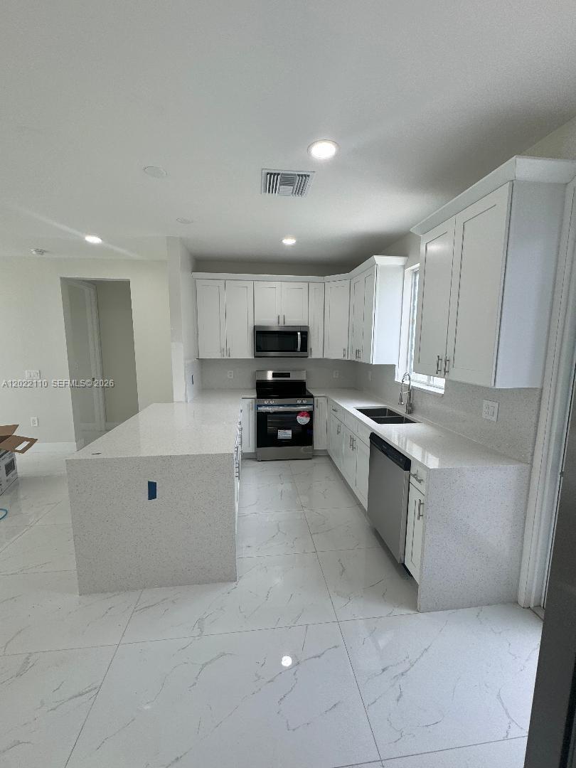 A modern kitchen features white cabinets, quartz countertops, stainless steel appliances, and light tile flooring — 55 S Colin ave, Lehigh Acres FL 33976, LEHIGH ACRES, FL