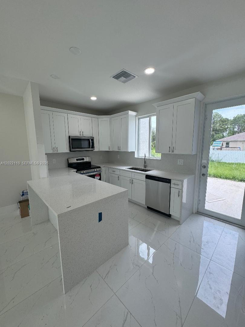 A modern kitchen features white cabinets, quartz countertops, a kitchen island, and light tile flooring — 55 S Colin ave, Lehigh Acres FL 33976, LEHIGH ACRES, FL