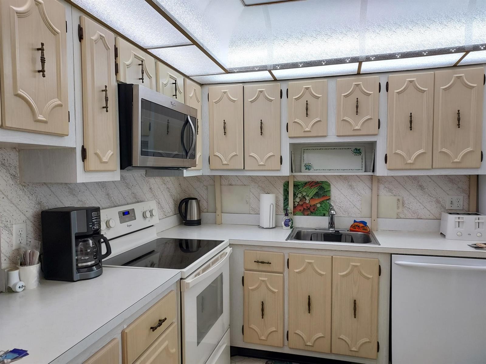 A kitchen features light wood cabinets, white countertops, a stainless steel microwave, and a drop-in sink — 717 S Us Hwy 1 Unit 309, Jupiter FL 33477, JUPITER, FL