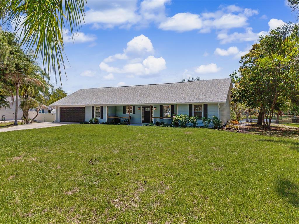 A single-story house with light-colored siding, a dark garage door, and a large front lawn — 601 136TH COURT E, BRADENTON, FL
