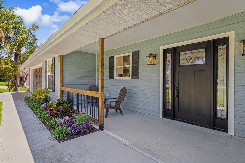 A light blue house exterior features a covered porch with a black door and chairs — 601 136TH COURT E, BRADENTON, FL