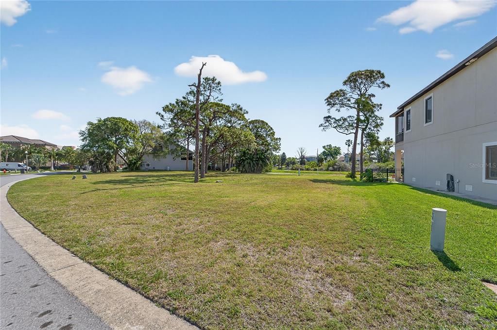 A grassy vacant lot sits next to a multi-story house under a blue sky — N POINTE ALEXIS DRIVE, TARPON SPRINGS, FL