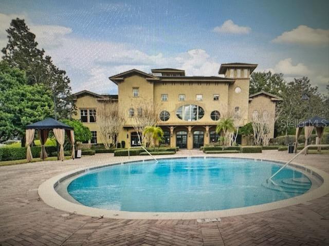 A large multi-story building stands behind a circular swimming pool and a small gazebo — 132 VISTA VERDI CIRCLE UNIT 100, LAKE MARY, FL