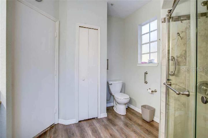 A bathroom features wood-look flooring, a white toilet, a glass shower, and a closet — 132 VISTA VERDI CIRCLE UNIT 100, LAKE MARY, FL