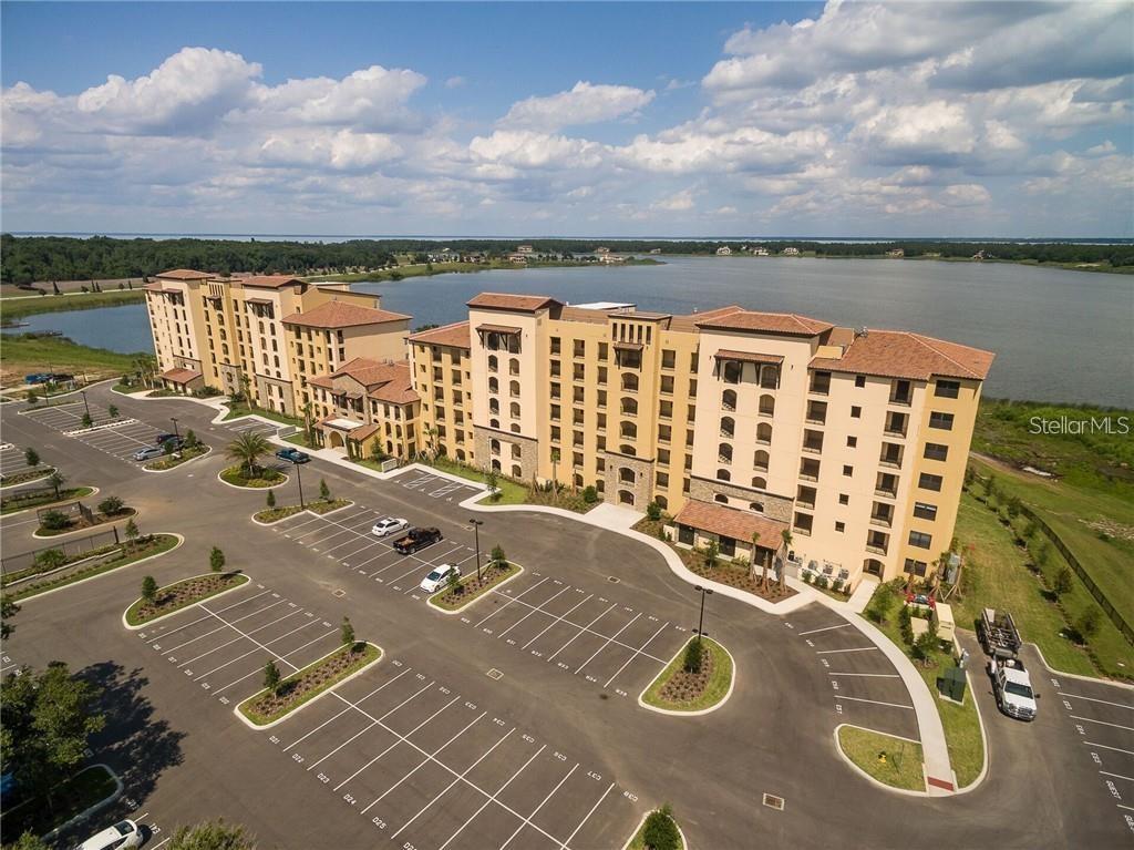 An aerial view shows a large multi-story apartment building with a parking lot and lake — 16300 COUNTY ROAD 455 UNIT 607, MONTVERDE, FL