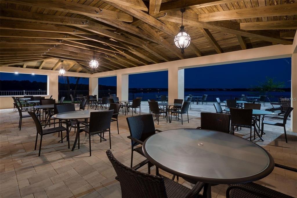 An outdoor covered patio features multiple dining tables and chairs overlooking a lake at night — 16300 COUNTY ROAD 455 UNIT 607, MONTVERDE, FL