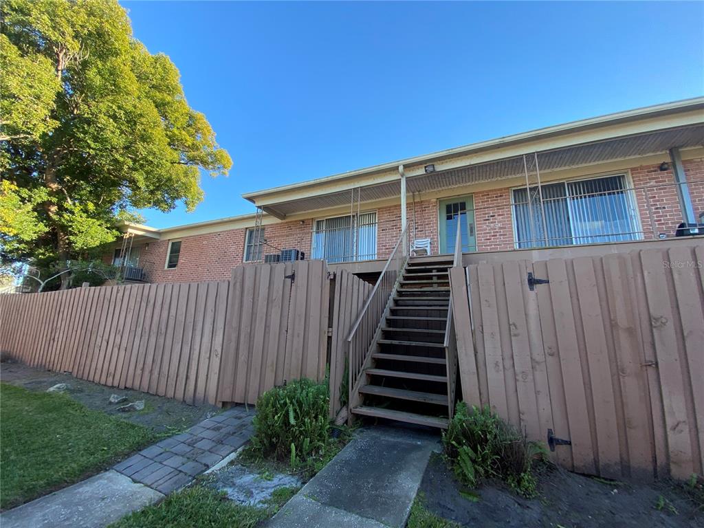 A brick apartment building features a wooden staircase leading to an elevated balcony and entrance — 525 GEORGETOWN DRIVE UNIT F, CASSELBERRY, FL