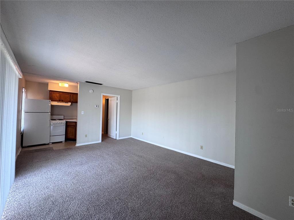 An open-concept living area features beige carpeting and a small kitchen with white appliances — 525 GEORGETOWN DRIVE UNIT F, CASSELBERRY, FL