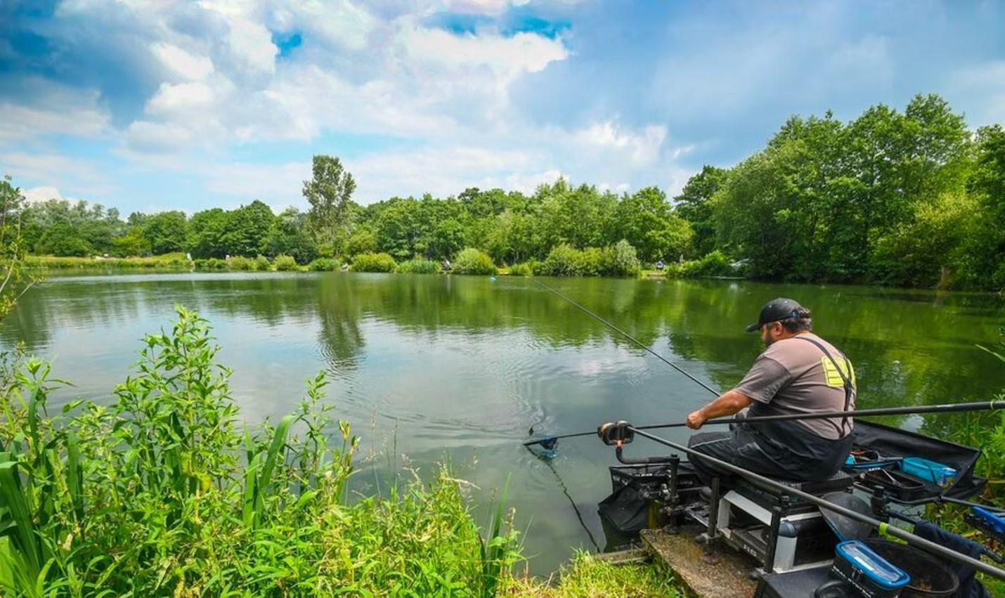 A man sits on a fishing platform by a calm lake surrounded by lush green trees — 523 Gloria Avenue, FL 32148, FL