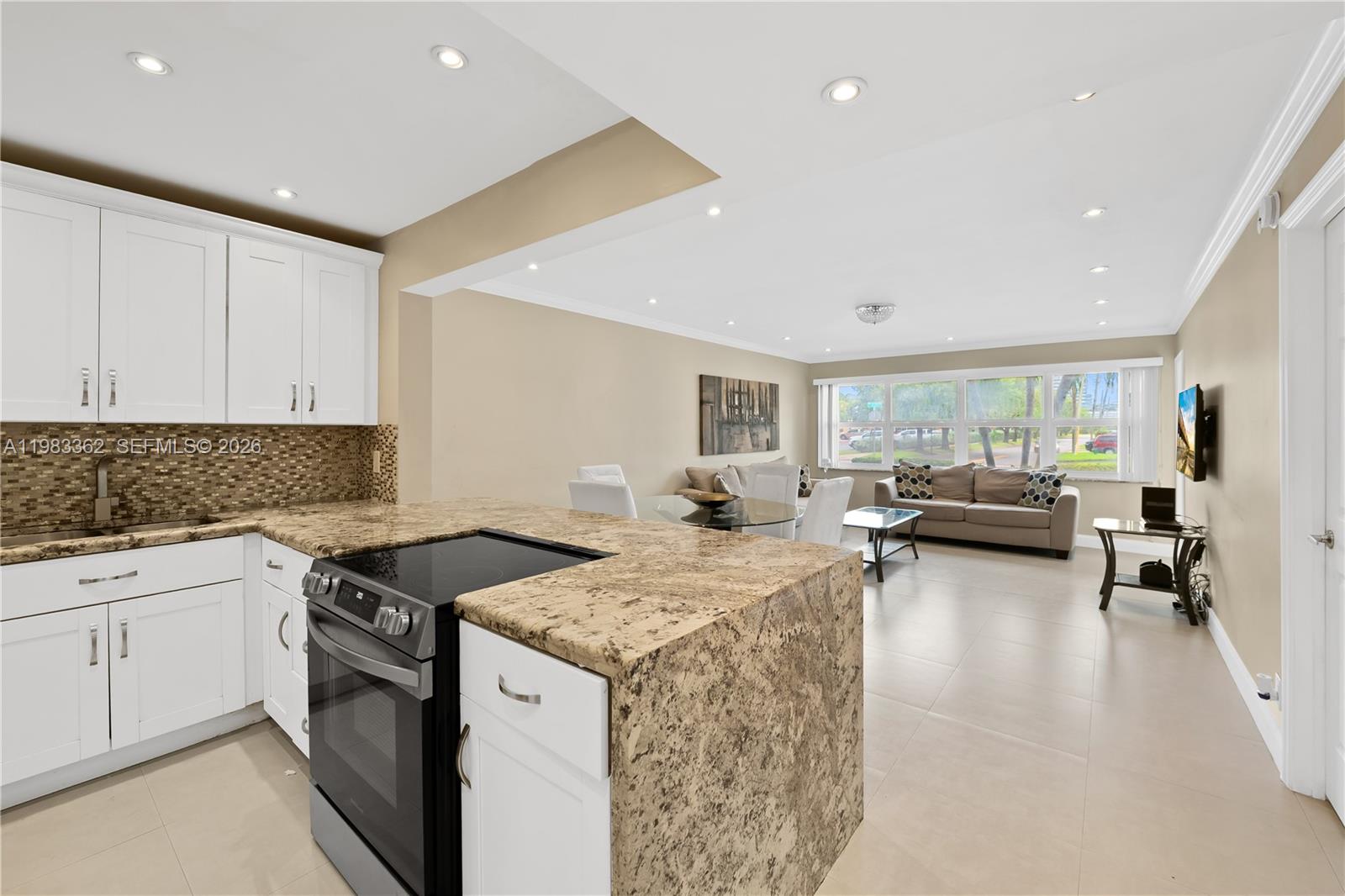A kitchen with granite countertops and white cabinets opens into a living and dining area — 329 SE 3rd St # 103S, Hallandale Beach FL 33009, HALLANDALE BEACH, FL