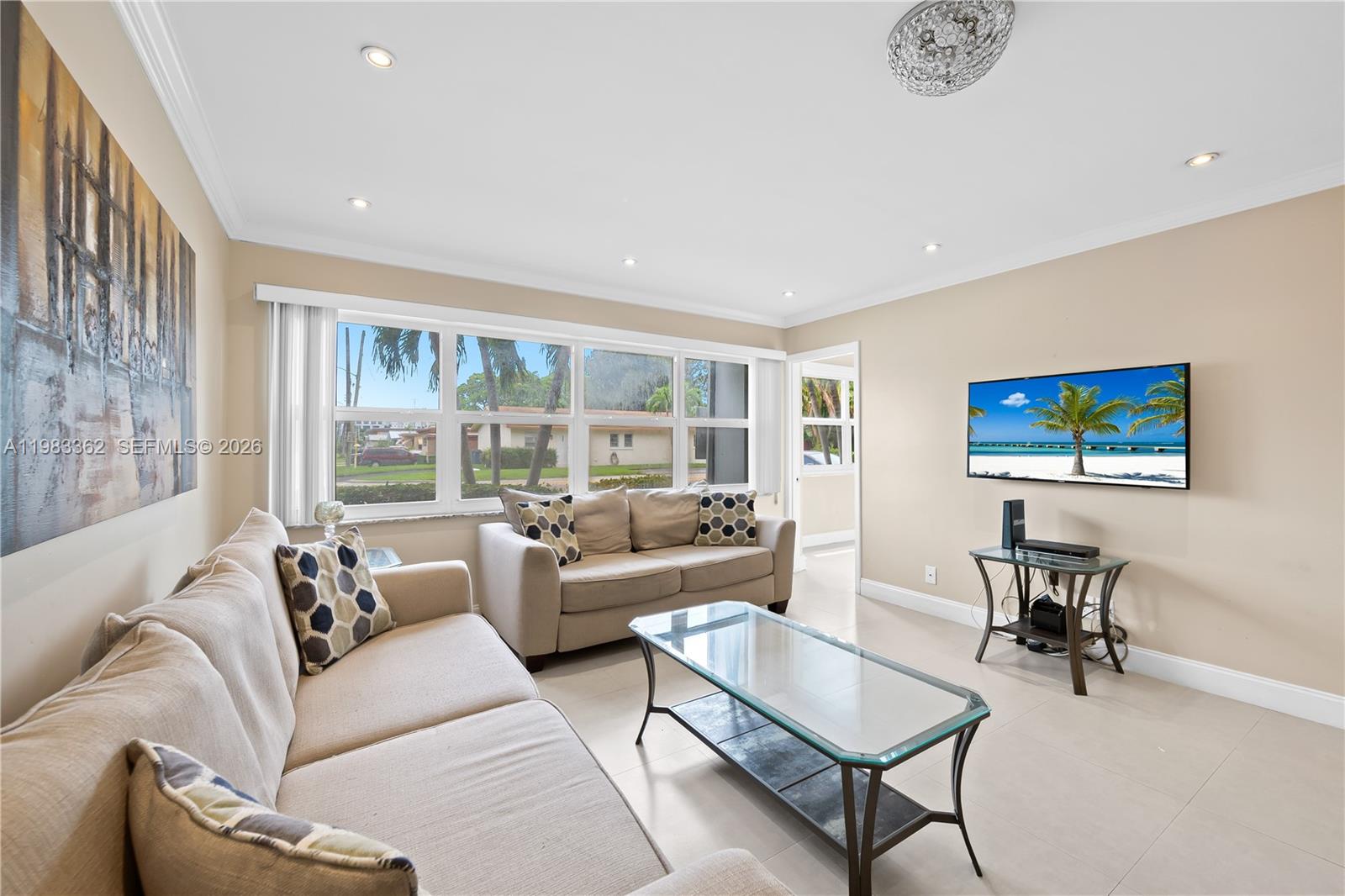 A living room features beige sofas, a glass coffee table, and a wall-mounted television — 329 SE 3rd St # 103S, Hallandale Beach FL 33009, HALLANDALE BEACH, FL