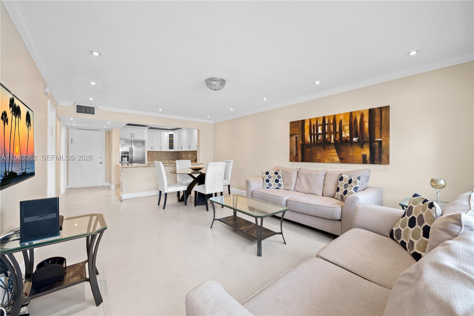 A living room with light tile floors, beige sofas, a glass coffee table, and a kitchen — 329 SE 3rd St # 103S, Hallandale Beach FL 33009, HALLANDALE BEACH, FL