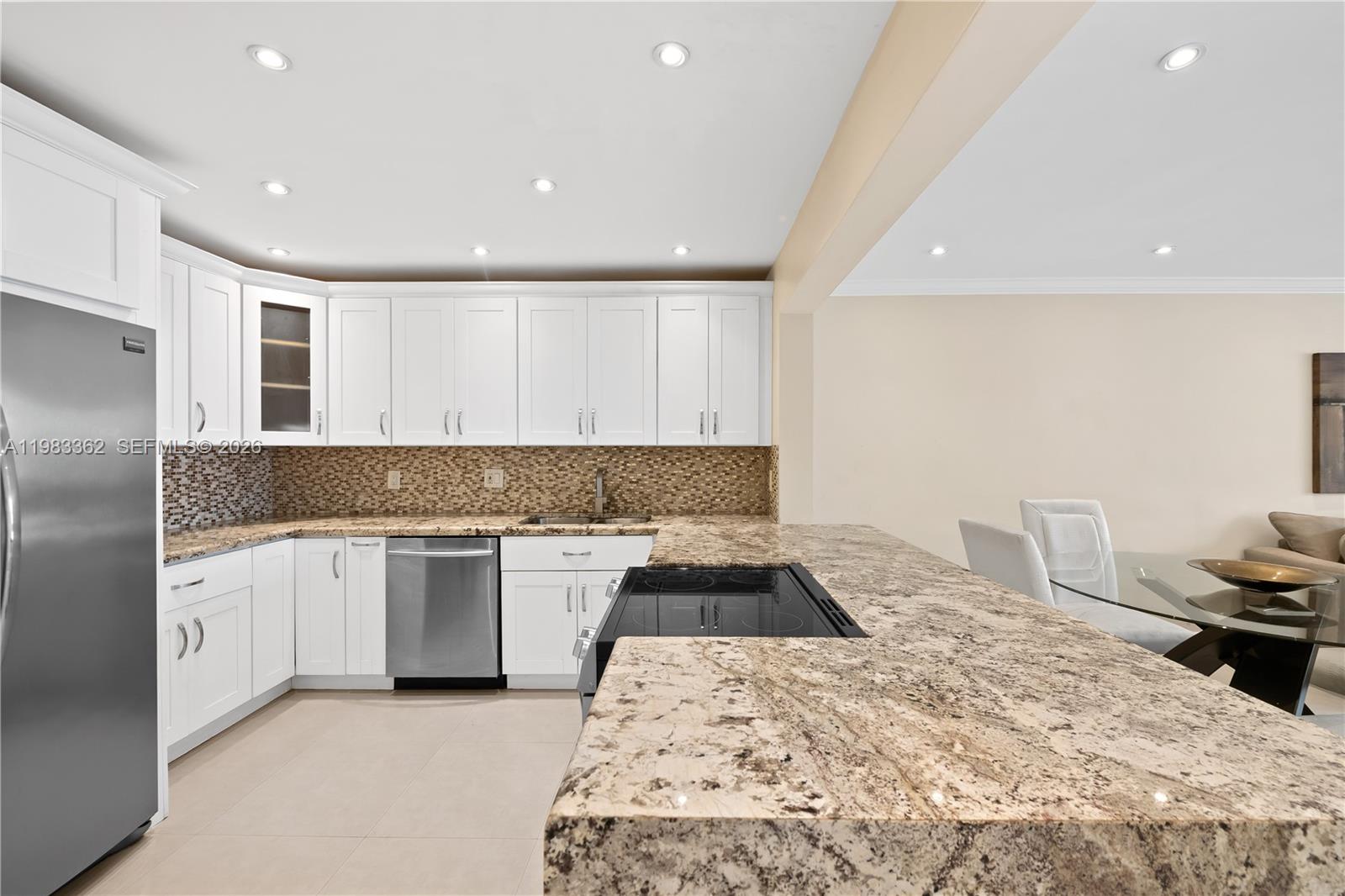 A kitchen features white cabinets, granite countertops, stainless steel appliances, and a tile backsplash — 329 SE 3rd St # 103S, Hallandale Beach FL 33009, HALLANDALE BEACH, FL