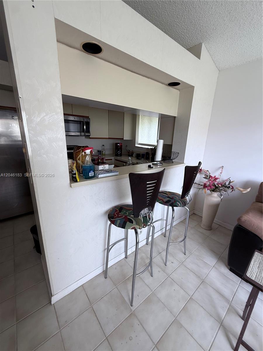 A kitchen pass-through window features a breakfast bar with two stools and tiled flooring — 11185 Rios Rd, Boca Raton FL 33498, BOCA RATON, FL