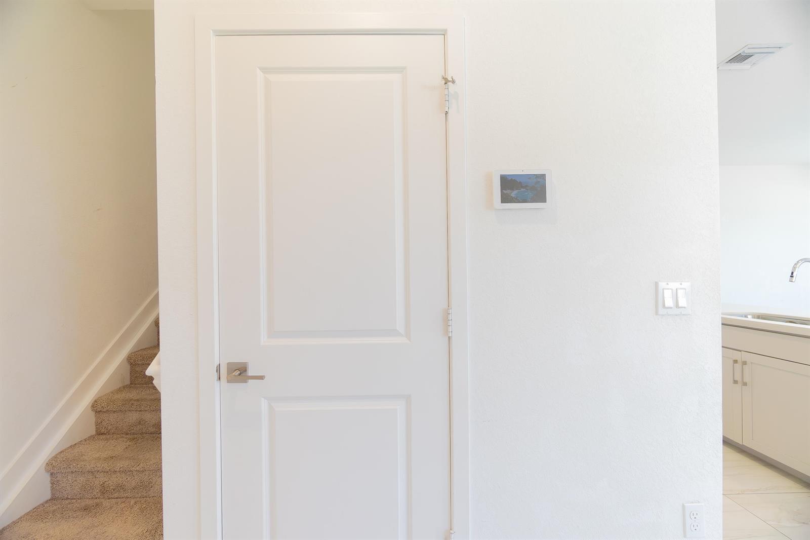 A white door stands next to a wall-mounted smart home display and a staircase — 8618 Via Mar Rosso, Lake Worth FL 33467, LAKE WORTH, FL