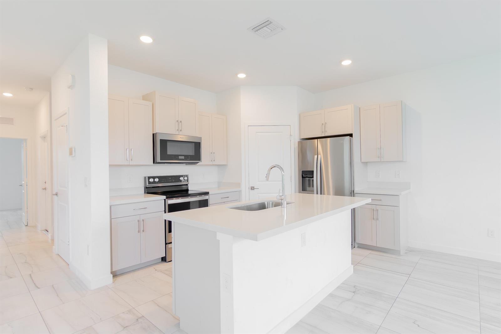 A modern kitchen features white cabinetry, stainless steel appliances, a center island, and tiled flooring — 8618 Via Mar Rosso, Lake Worth FL 33467, LAKE WORTH, FL