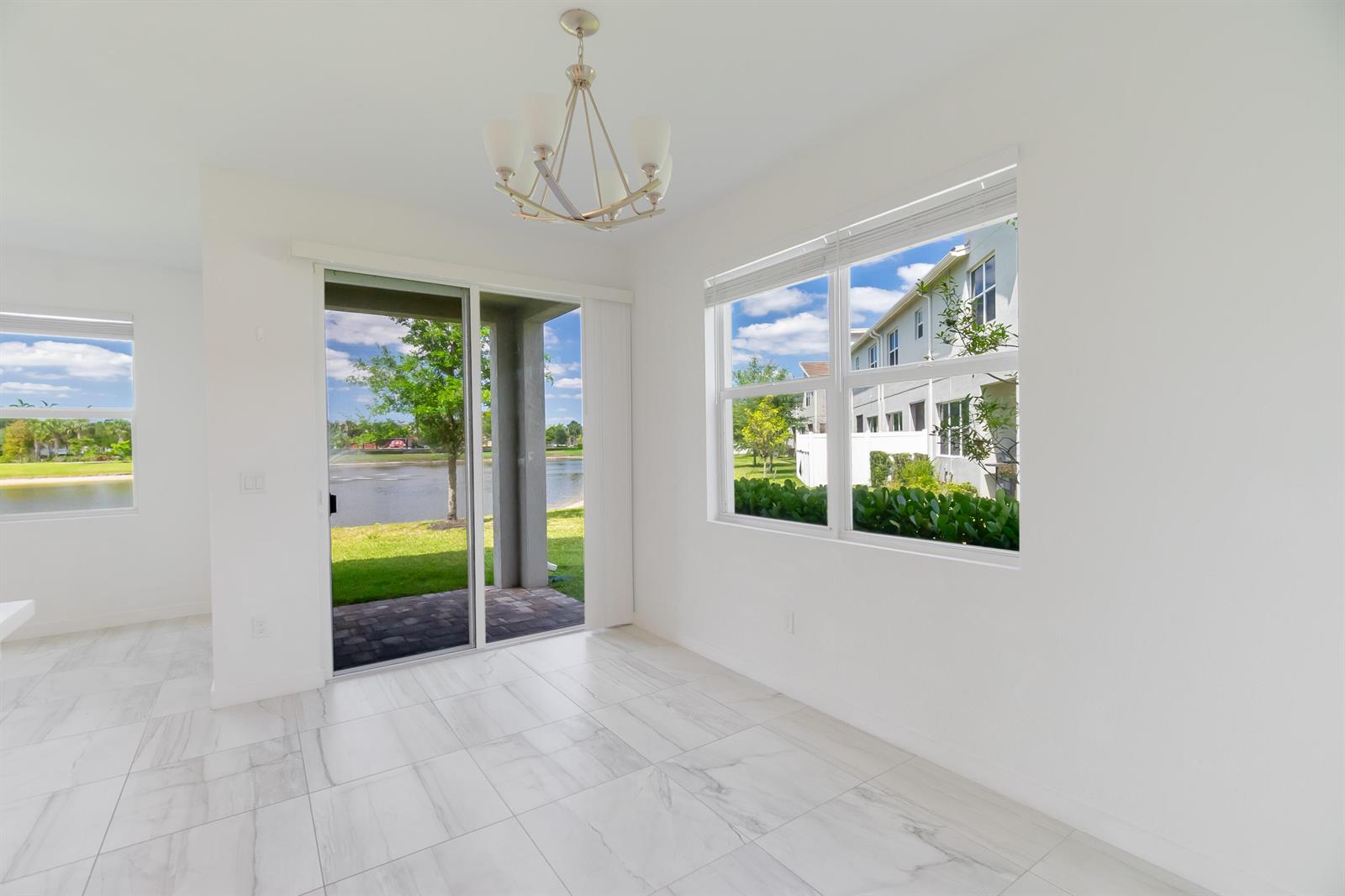 A bright dining area features white tile floors, a chandelier, sliding glass doors, and windows — 8618 Via Mar Rosso, Lake Worth FL 33467, LAKE WORTH, FL